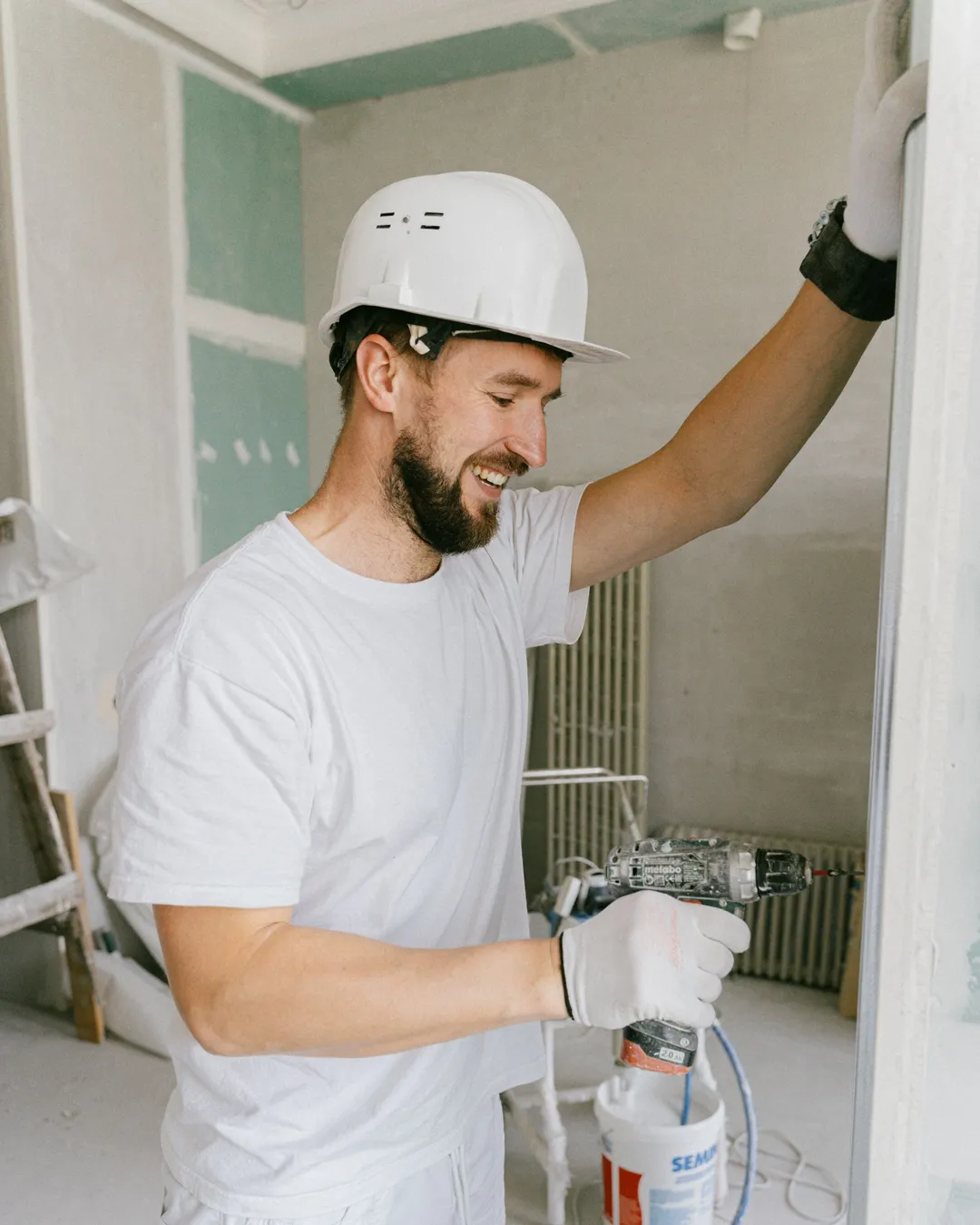 Artisan souriant en casque et tenue blanche sur un chantier de rénovation
